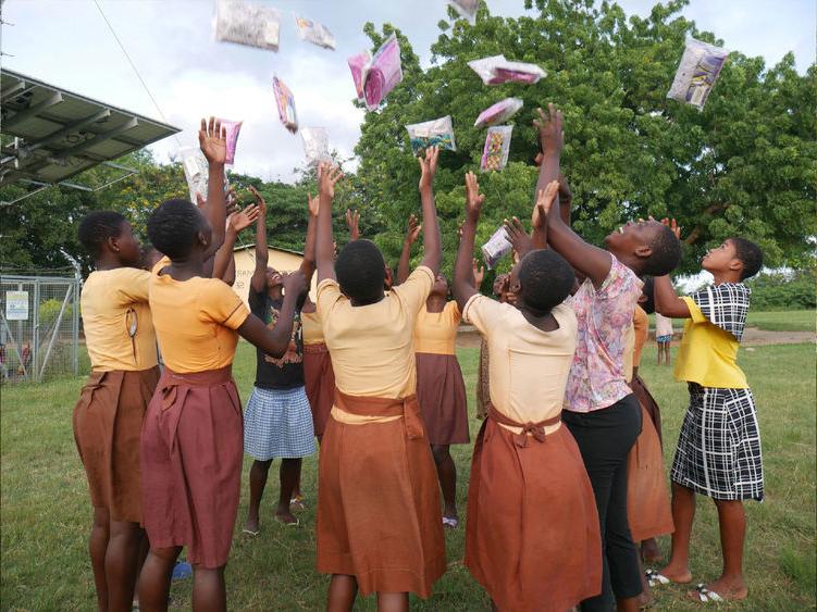 Students in Ghana throw period products in the air